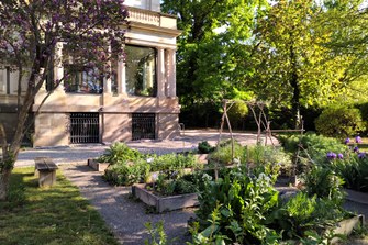 Titel Alternativtext: Blumenbeete des Gartens des Althochdeutschen Wörterbuchs mit Akademiegebäude im Hintergrund