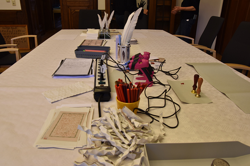 Im Vordergrund sind gefaltete Fidibusse zu sehen. Das sind kleine Briefe, die durch eine bestimmte Faltungsform nicht unerkannt geöffnet werden konnten und so bestens für den Austausch geheimer Nachrichten geeignet waren. Auf diese Weise gefaltetes Papier wurde auch benutzt, um Pfeifen anzuzünden.