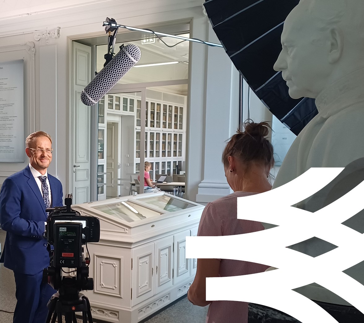 Eine Person gibt ein Interview, man sieht Mikrofone und Kameras, im Hintergrund Bücherwände und Ausstellungsvitrinen des Goethe- und Schiller-Archivs. Im unteren Bildrand sieht man einen Ausschnitt des Akademielogos.