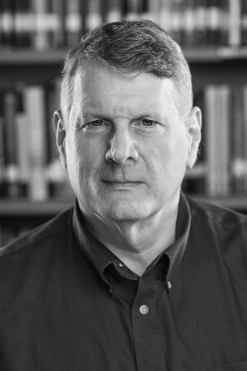 Schwarz-weiß-Porträtfoto einer männlichen Person vor einem Bücherregal